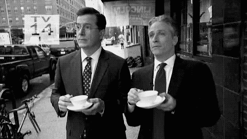 John Stewart and Stephen Colbert sipping from fancy tea cups in the street and remarking ‘Wow’ and ‘Bravo’ at something happening offscreen